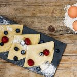 Crepes senza lattosio con latte di mandorla: ricetta facile con video 1 su base di legno e tagliere nero si vedono tre crepes con frutti di bosco