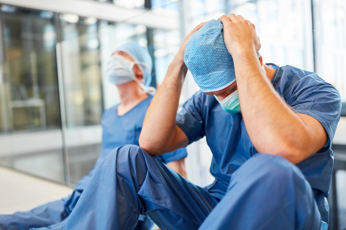 Sindrome da burnout: sintomi, cause e come prevenire lo stress lavoro-correlato 2 un infermiere seduto per terra che si prende la testa tra le mani in pieno burnout