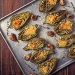 Carciofi ripieni senza carne al forno e in padella 1 su tavolo da cucina, teglia da forno con vari carciofi ripieni con erbe aromatiche