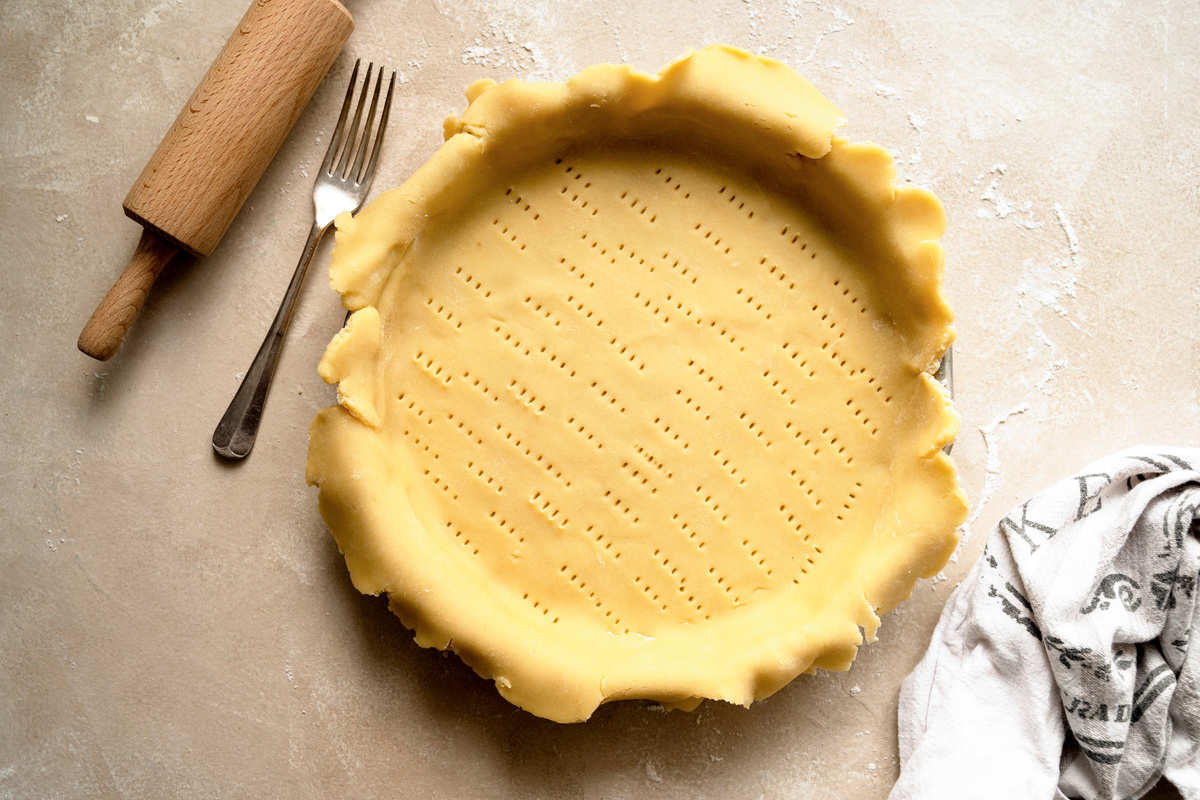 Pasta frolla classica: ingredienti e varianti per dolci favolosi 1 in primo piano su uno stampo rotondo, è stesa la pasta frolla con dei piccoli fori per ottimizzare la cottura in forno
