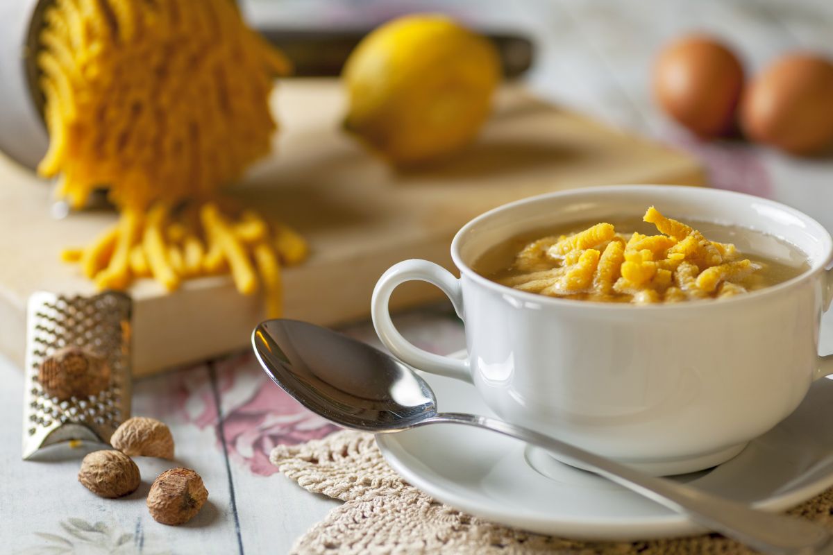 Minestre e zuppe: ricette da gustare quando fa freddo e non solo 24 tazza bianca su piattino con una porzione di passatelli in brodo, cucchiaio, noce moscata e tagliere con limone e pasta