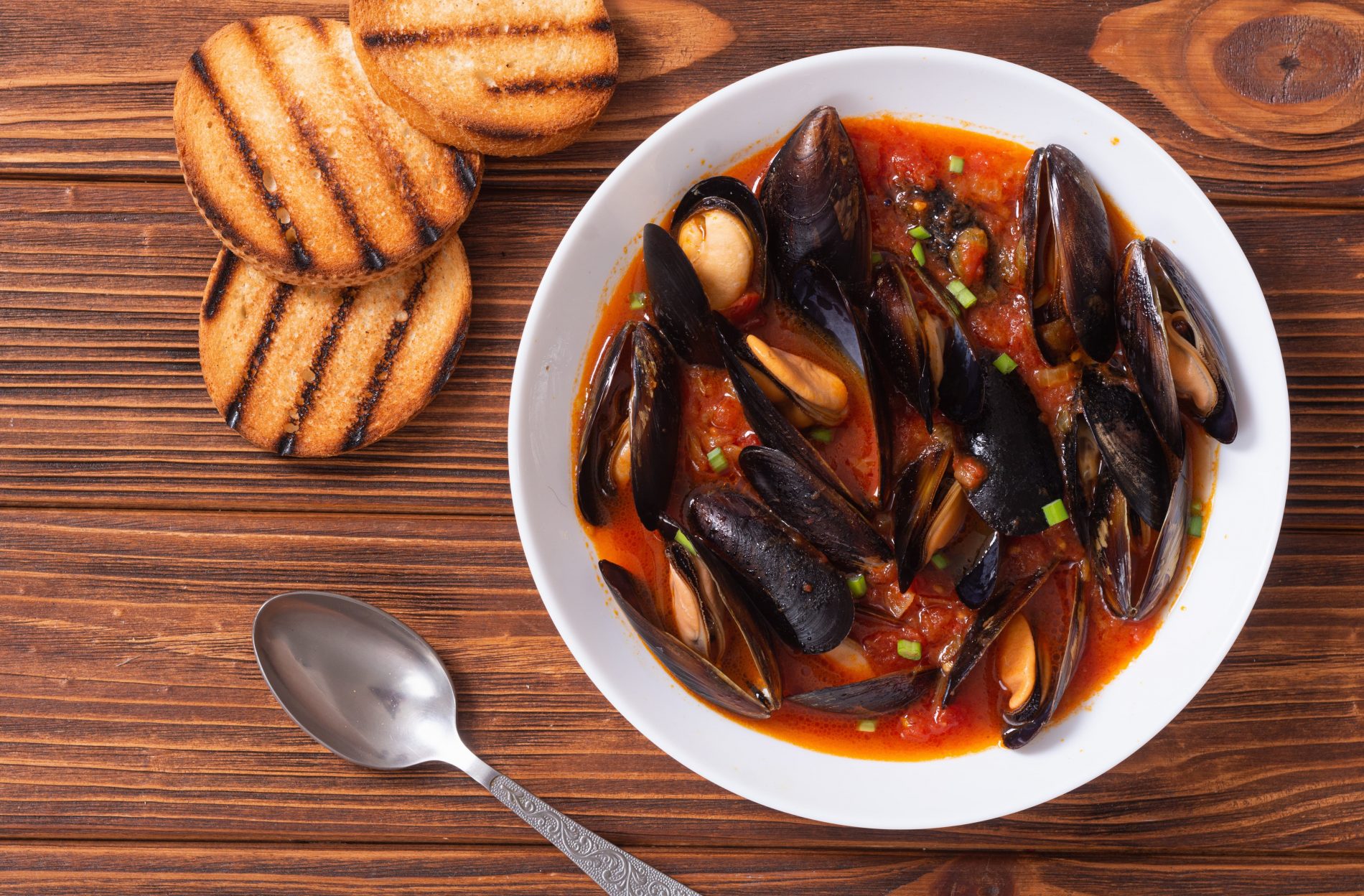 Minestre e zuppe: ricette da gustare quando fa freddo e non solo 18 piatto bianco su un tavolo di legno con una zuppa di cozze, un cucchiaio e 3 fette di pane tostato