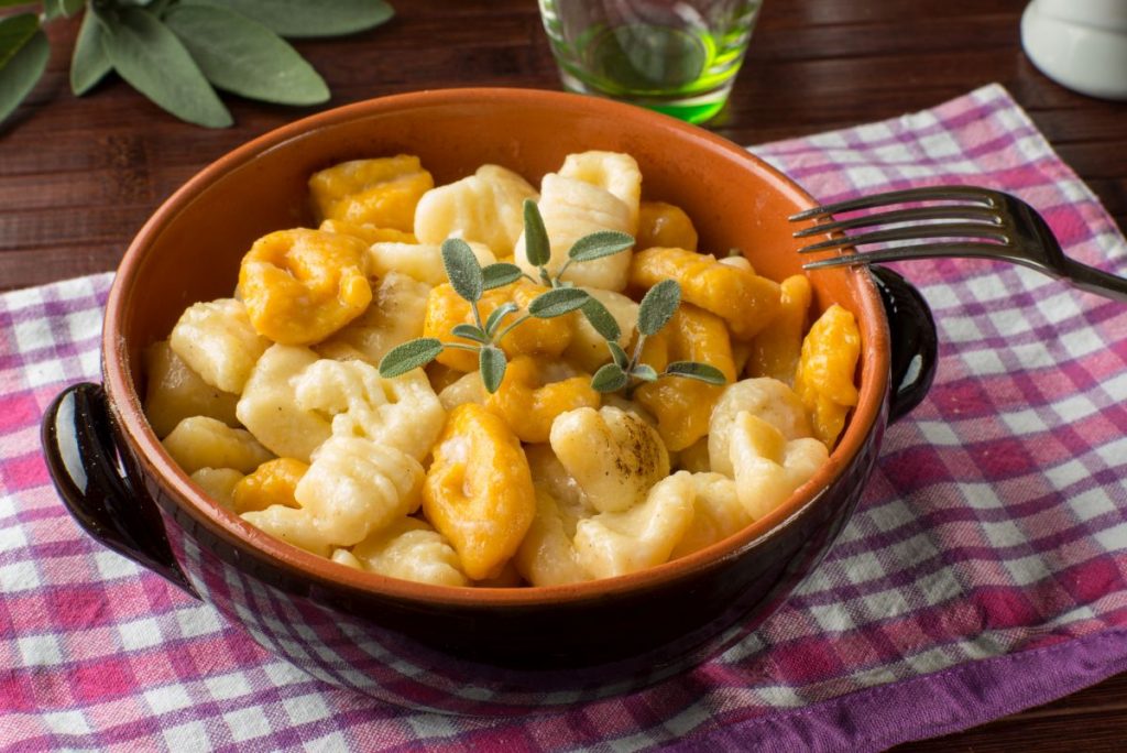 Gnocchi di zucca: condimenti, ricetta base e varianti 3 in primo piano su un tavolo con una tovaglia rustica, una cocotte di terracotta con i gnocchi di zucca e ricotta.
