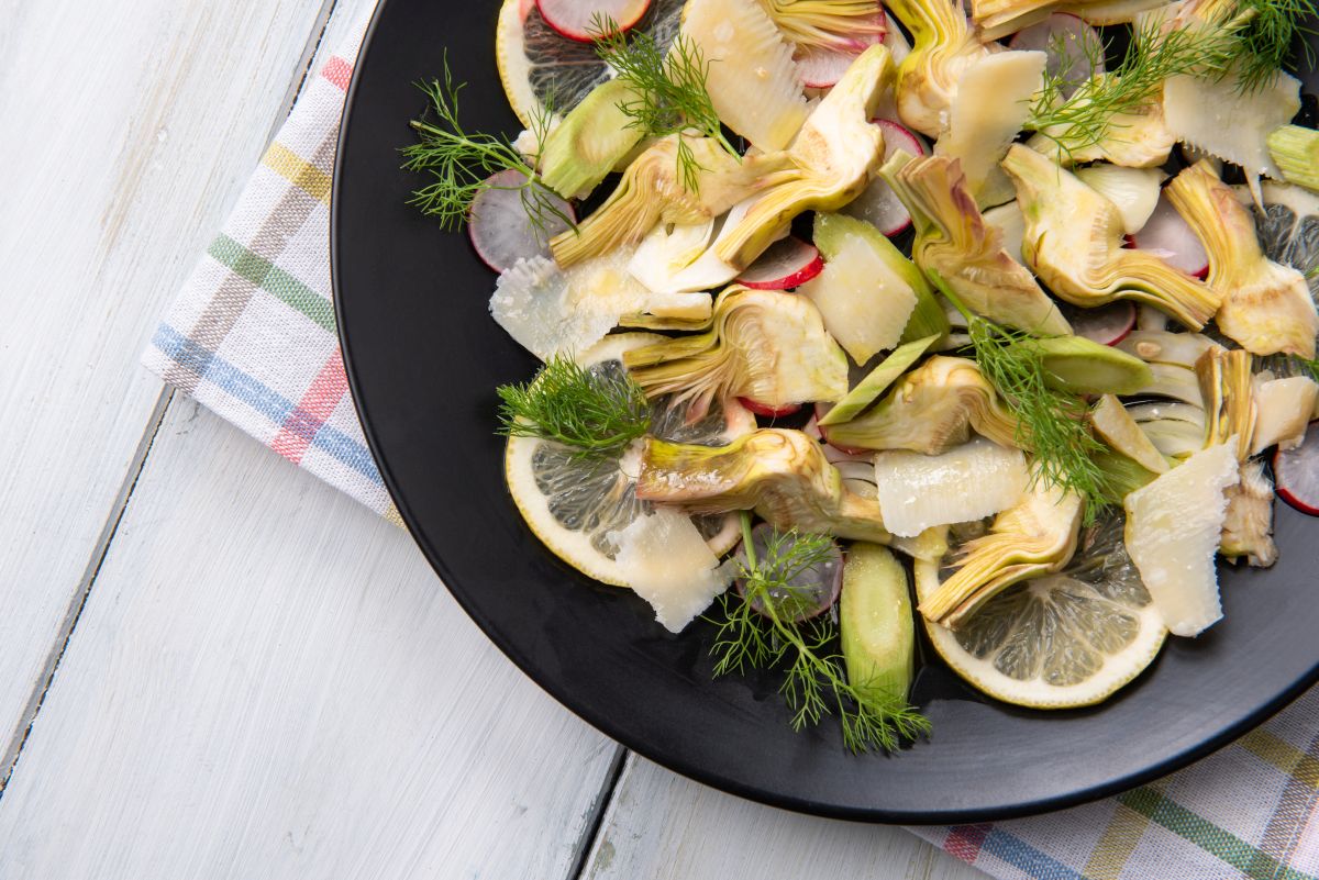Insalata di carciofi, un contorno sano, leggero e nutriente 2 su tavolo da cucina, piatto nero con insalata di carciofi crudi