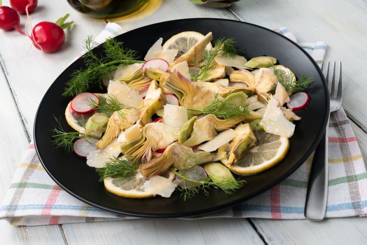 su tavola apparecchiata piatto tondo nero con Insalata di carciofi