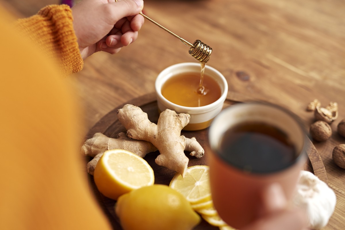 Tisana zenzero e limone: proprietà, benefici e ricetta 2 una mano femminile che addolcisce la tisana zenzero e limone con il miele