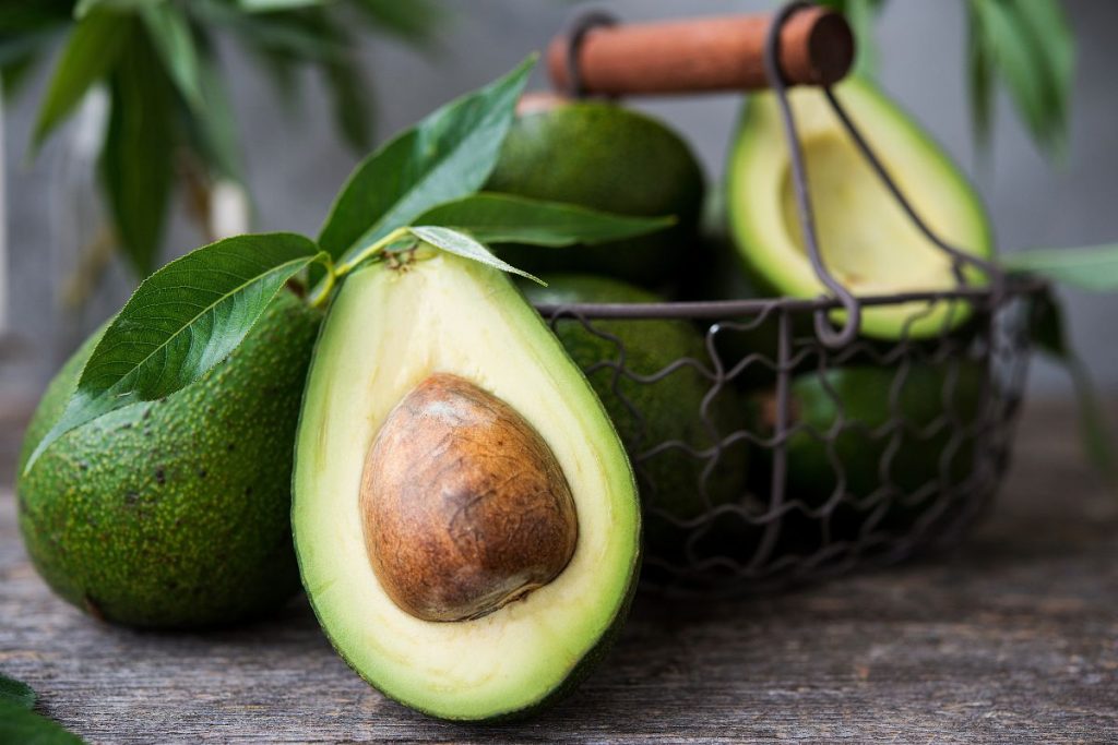 Mangiare un avocado al giorno fa bene? 1 mangiare un avocado al giorno: un cestello con alcuni avocado verdi, un avocado tagliato a metà in primo piano