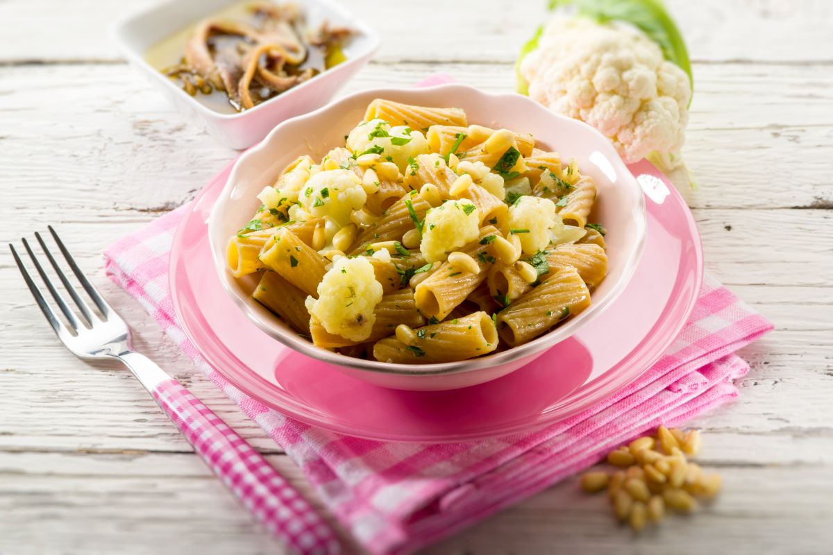 Ricette con cavolfiore: idee facili e creative dall'antipasto al contorno 2 su tovagliolo a quadri rosa, sottopiatto rosa e scodella piena di rigatoni con cavolfiore