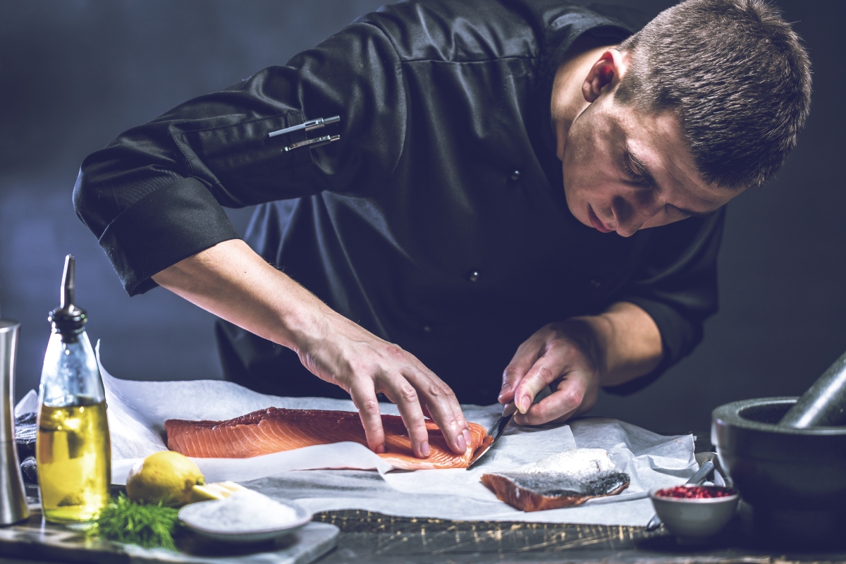 Salmone: calorie, ricette, differenze tra fresco e affumicato e valori nutrizionali 3 Uno chef che taglia a fette sottili un grande trancio di salmone affumicato