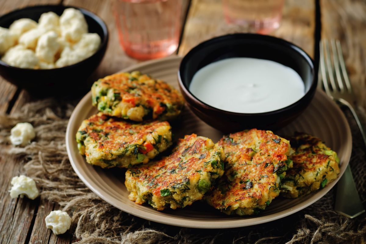 ricette con cavolfiore: piatto tondo con 5 frittelle di cavolfiore e una ciotola nera con della salsa bianca
