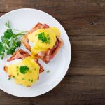 Uova alla Benedict, un goloso piatto americano per la tua colazione 2 su base di legno un piatto tondo bianco con sopra due uova alla Benedict