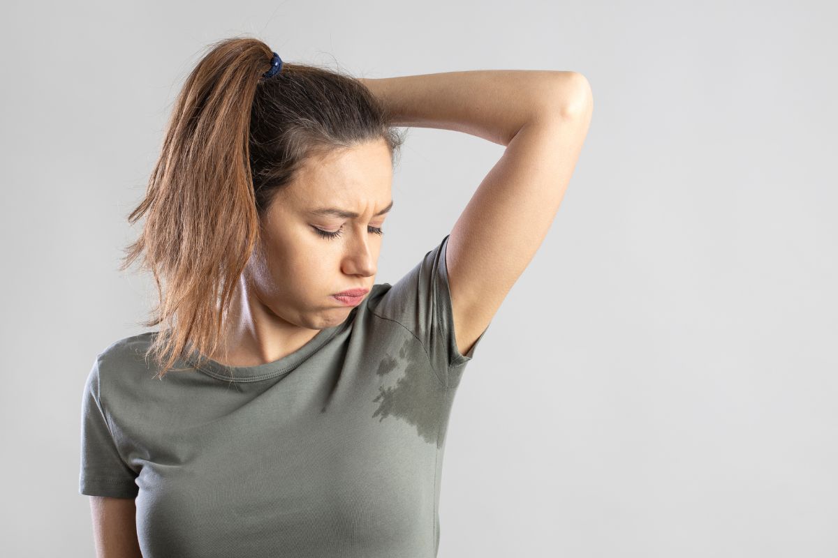 Come non sudare (soprattutto in estate)? Ecco alcuni semplici rimedi 1 Una giovane donna che osserva la maglietta macchiata di sudore sotto le ascelle