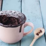 Mug cake senza uova e senza burro pronta in 2 minuti 1 su base di legno celeste una tazza rosa con dentro la mug cake e un cucchiaino