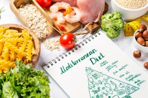 Iscriviti subito alla dieta Melarossa e scarica l'app 20 alcuni cibi come pasta, pesce e verdure su una tavola con in primo piano un'immagine della piramide alimentare