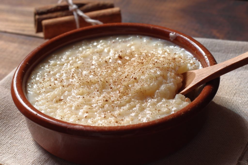 Riso al latte cremoso: un primo piatto semplice e veloce 2 primo piano di una ciotola di terracotta cn riso al latte e cannella, con dietro stecche di cannella