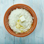 Riso al latte cremoso: un primo piatto semplice e veloce 1 su tavolo di legno azzurro una ciotola di terra cotta con riso al latte saltato con burro e formaggio