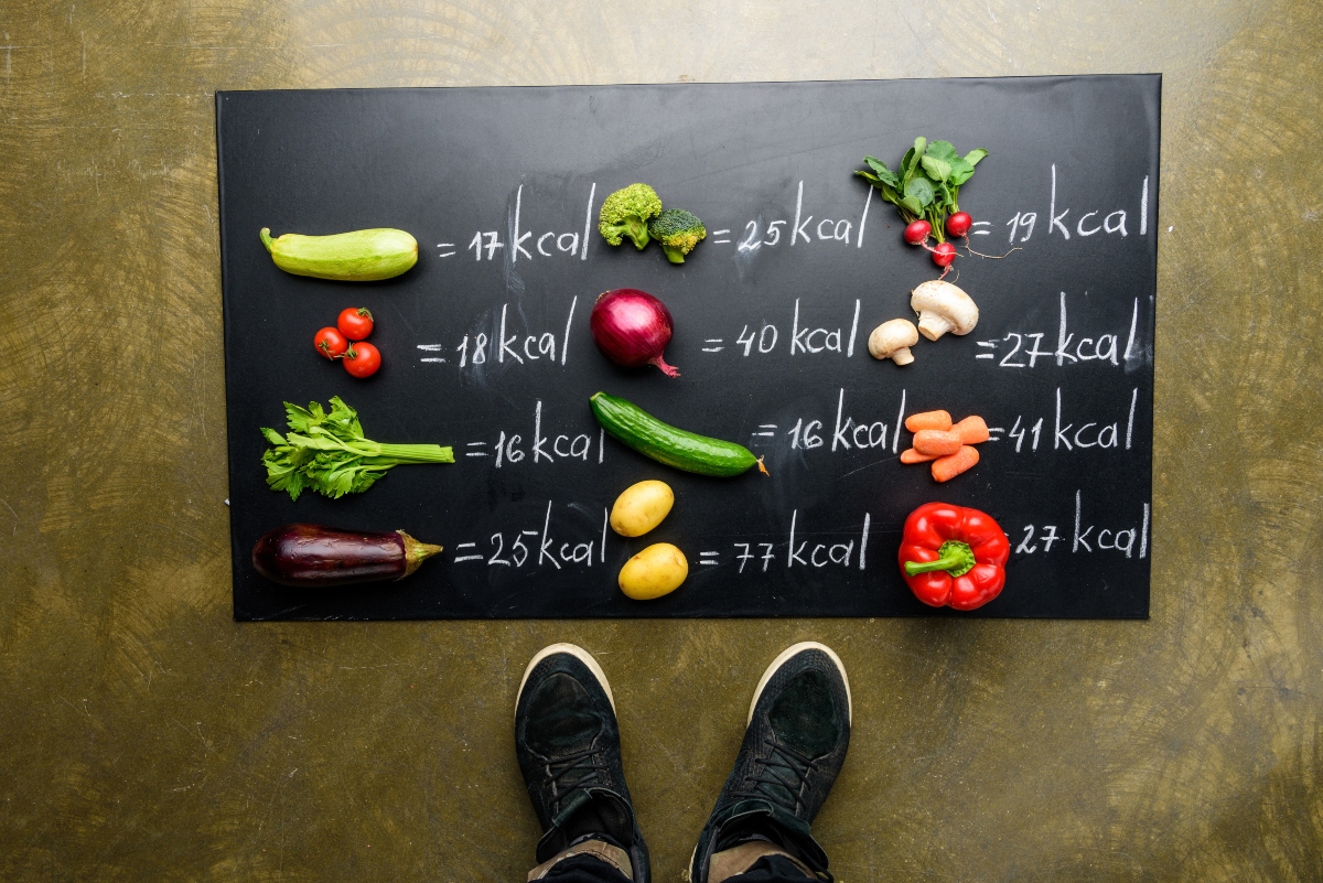 Metabolismo basale: cos’è e come si calcola 4 Una lavagna nera con dei frutti e verdure attaccati e il numero delle calorie scritte con il gesso
