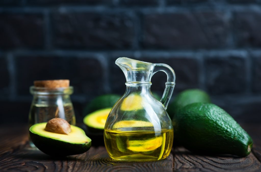 Proprietà dell'avocado: un superfood tutto da scoprire 1 una boccetta in vetro che contiene olio di avocado con un frutto spaccato a metà