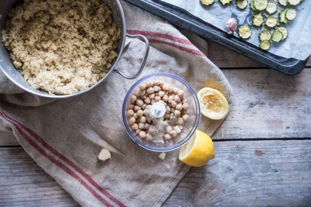 Buddha bowl con quinoa: la ricetta veloce per un piatto unico sano e gustoso 6 In primo piano all'interno di un frullatore dei ceci per preparare l'hummus come salsa della Buddha bowl, accanto dei spicchi di limone e la pentola con della quinoa.