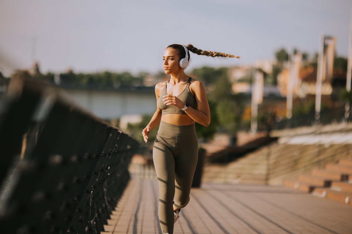 corsa per principianti: una bellissima donna con leggings e top beige e le cuffie sta iniziando a correre su un ponte