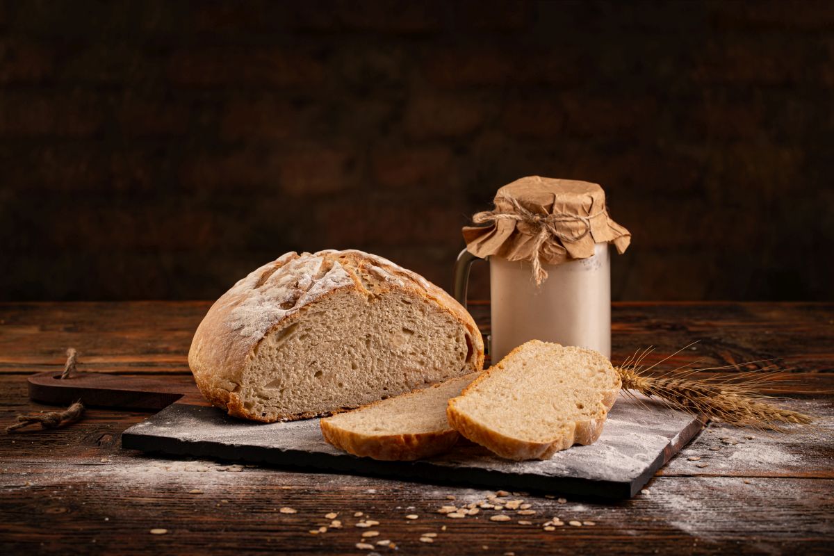 Pane fatto in casa: ricette genuine e semplici da provare 14 tagliere di legno con un pane e fette e un barattolo