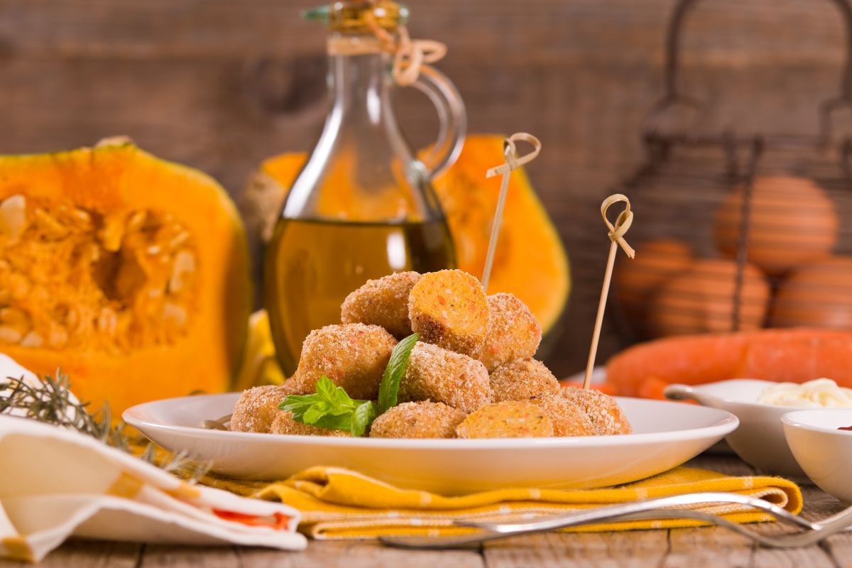 Ricette con la zucca: le migliori idee sane e gustose 12 piatto bianco con polpette di zucca e spiedini, zucca aperta e flacone di olio sullo sfondo