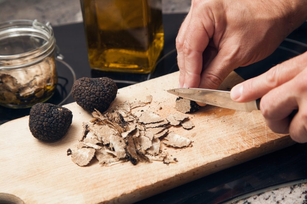 Tartufo: cos’è, quanto costa e perché è così pregiato 1 in primo piano una mano maschile che affetta un tartufo nero