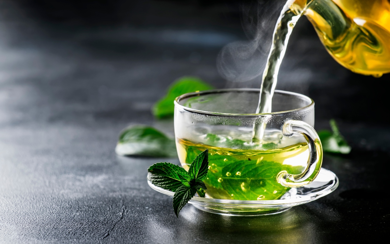 Tè verde: benefici, proprietà e quanto berne al giorno 8 tè verde e una teiera che versa la bevanda in una tazza trasparente