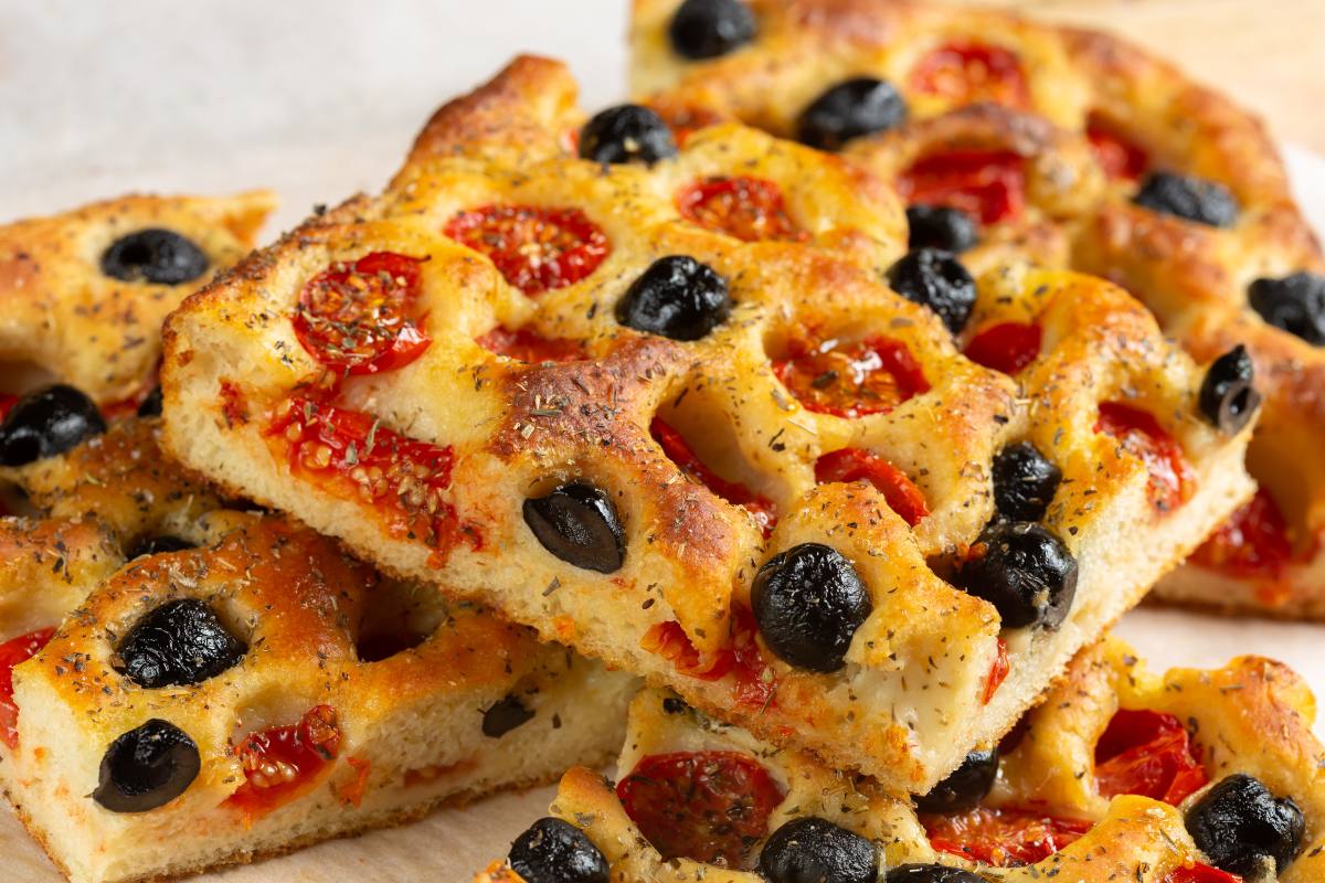 Ricette focaccia: ricetta base e 10 varianti irresistibili da fare in casa 4 primo piano di alcune fette di focaccia pugliese con pomodorini e olive