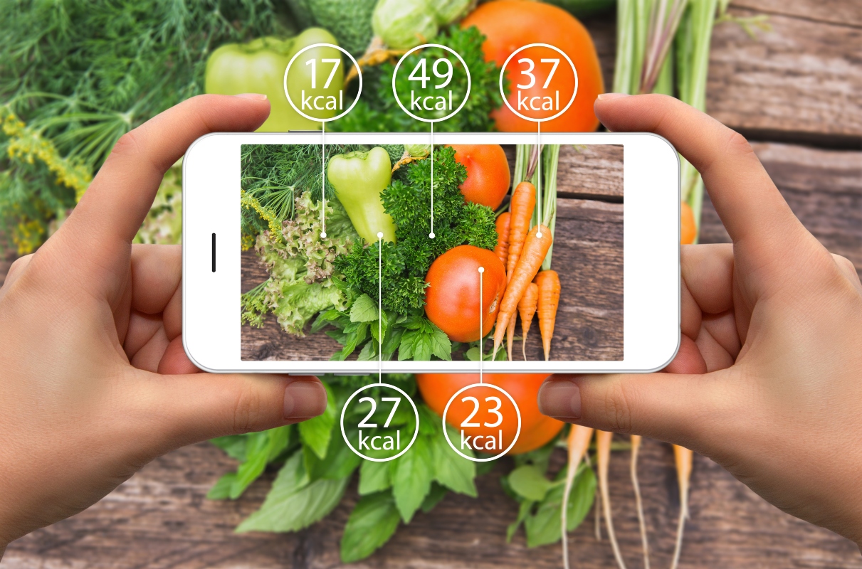 Fabbisogno calorico due mani che reggono uno smartphone che inquadra alcuni alimenti