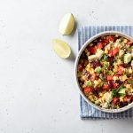 Quinoa con verdure: ricetta leggera e senza glutine 1 Im primo piano su un tavolo di marmo bianco in un piatto fondo c'è della quinoa con verdure. Sulla destra una forchetta e in alto a sinistra due spicchi di lime.