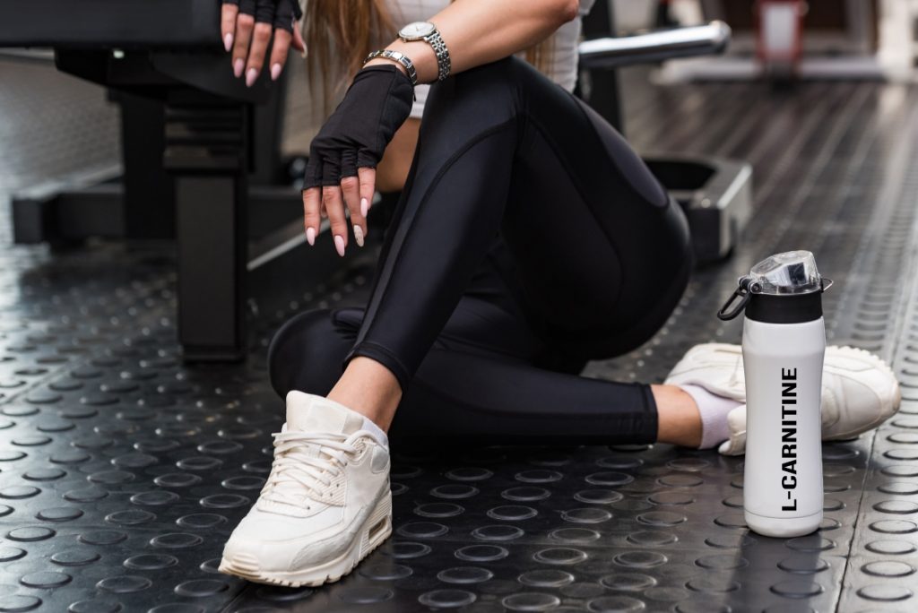 Carnitina: a cosa serve, benefici e quando prenderla 2 una giovane donna in palestra che tiene in mano una borraccia con la scritta L-carnitina