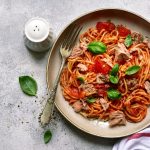 Pasta al tonno con pomodoro: la ricetta veloce con video 1 in primo piano su un piatto fondo degli spaghetti al tonno con pomodoro e qualche foglia di basilico