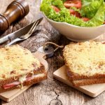 Croque monsieur,il famoso sandwich francese, ricetta classica e varianti più leggere 1 su tavolo di legno due toast croque monsieur accanto a una scodella di insalata e un macina pepe