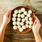 Polpette di ricotta al forno: la ricetta di un secondo piatto vegetariano 1 su tavolo di legno. mani di una donna che fa vedere una ciottola con diverse polpette di ricotta prima di infornarle