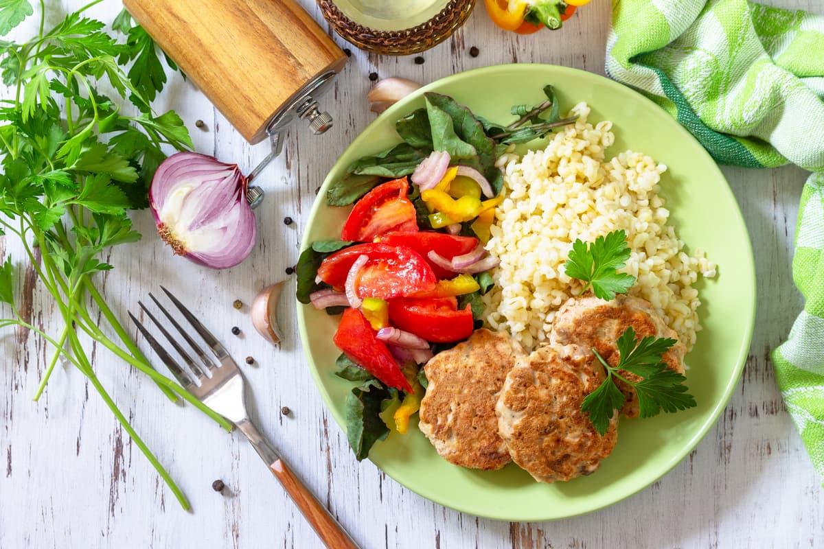 17 ricette con tonno fresco e tonno in scatola veloci e saporite 2 su tavolo bianco di legno un piatto verde con polpette di tonno, riso e peperoni. Attorno aglio, 1 forchetta e pepe macinato