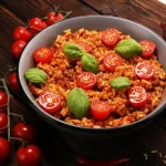 Risotto al pomodoro, come farlo cremoso e gustoso anche con la ricetta Bimby 2 padella tonda con risotto al pomodoro e foglie di basilico, pomodorini e cipolle rosse intorno