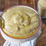 Polenta taragna: un piatto nutriente della tradizione valtellinese 1 su tavola di legno, ciotola con la polenta taragna e un cucchiaio, accanto un bicchiere di farina di grano saraceno. Sotto la ciotola, c'è un canovaccio bianco