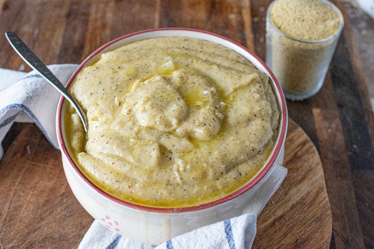 su tavola di legno, ciotola con la polenta taragna e un cucchiaio, accanto un bicchiere di farina di grano saraceno. Sotto la ciotola, c'&egrave; un canovaccio bianco