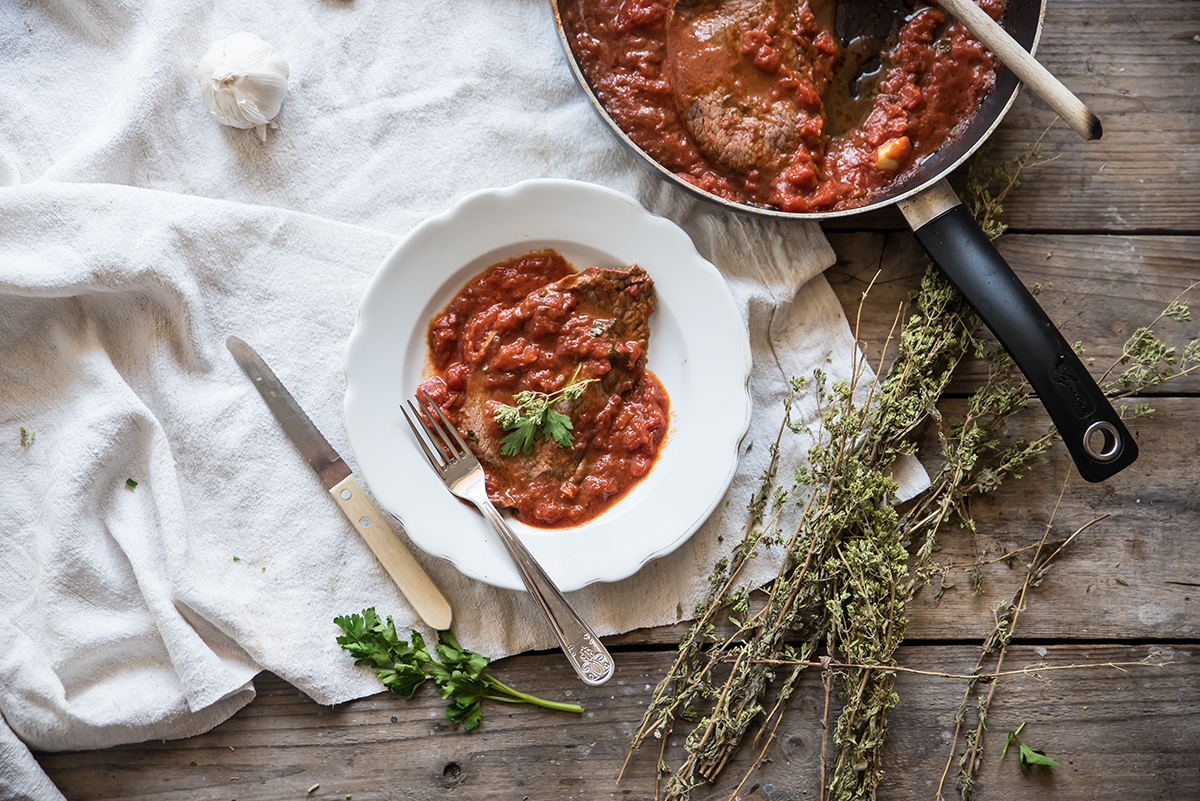 padella con manico e piatto tondo bianco con carne alla pizzaiola