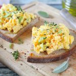Uova strapazzate: cottura perfetta e varianti semplici da provare 2 in primo piano su una fetta di pane delle uova strapazzate con delle erbe aromatiche