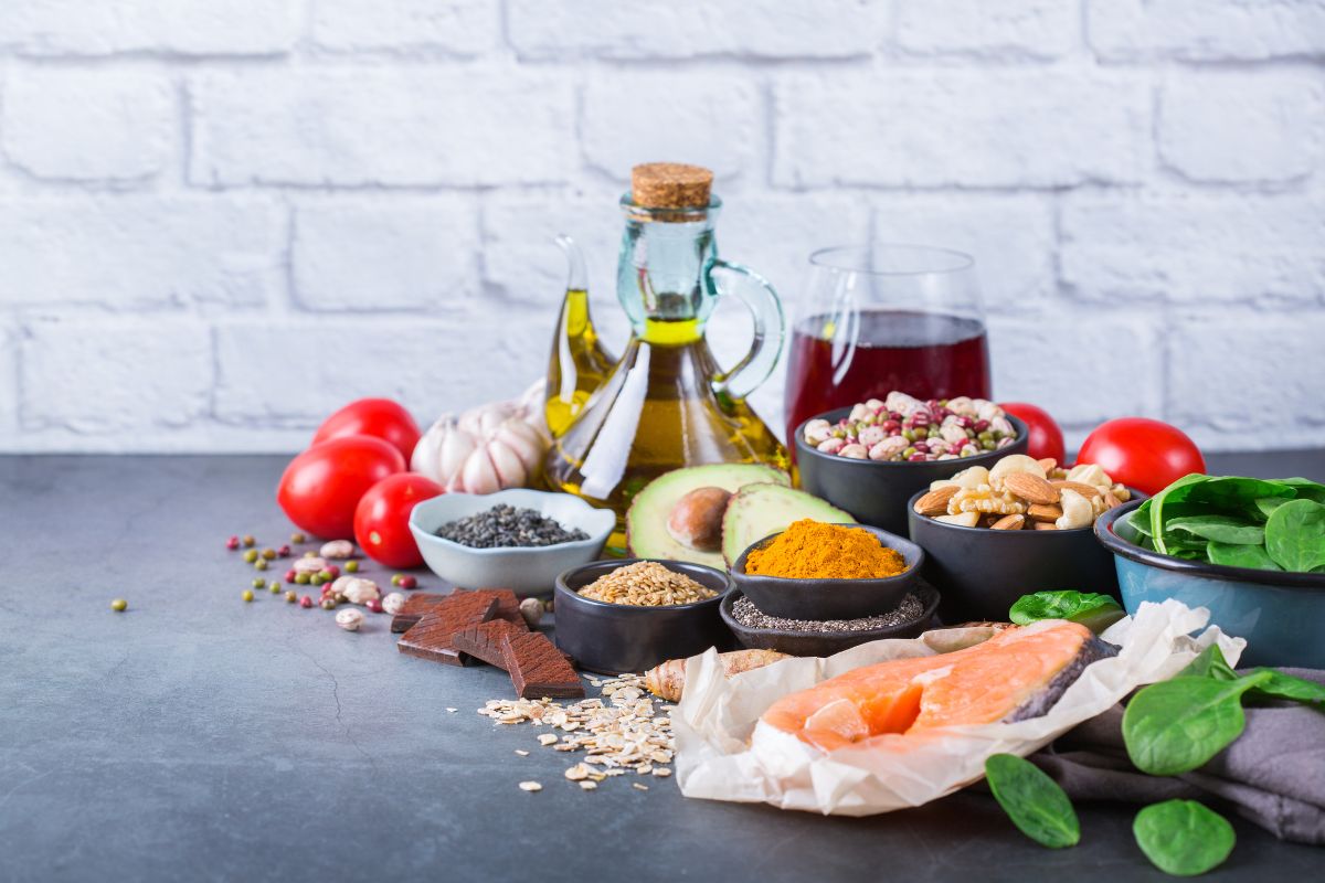 Cibi antinfiammatori: 8 alimenti da inserire nella dieta 1 Alcuni alimenti su un tavolo come una fetta di salmone, pomodorini, semi vari e una bottiglia di olio di oliva