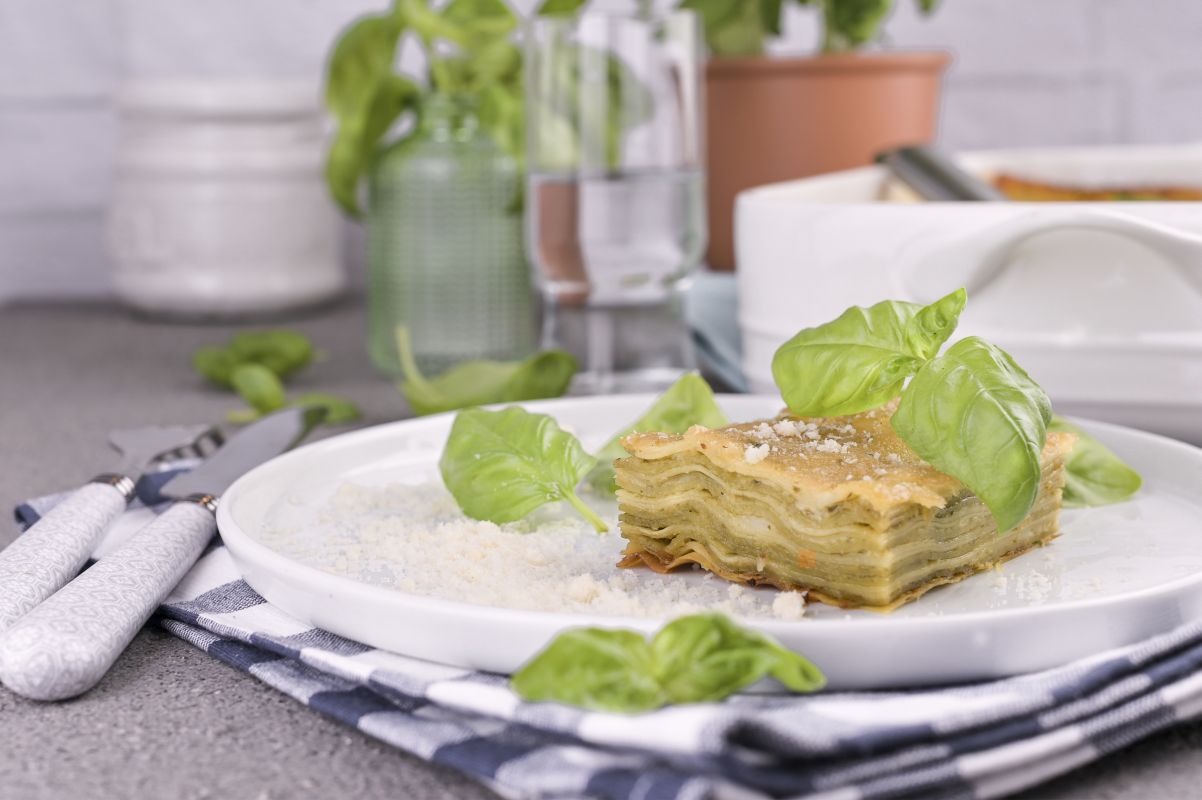 Le migliori ricette vegetariane: idee facili e gustose 6 Ricetta per i vegetariani: un piatto piano con una porzione di lasagne al pesto e foglie di basilico