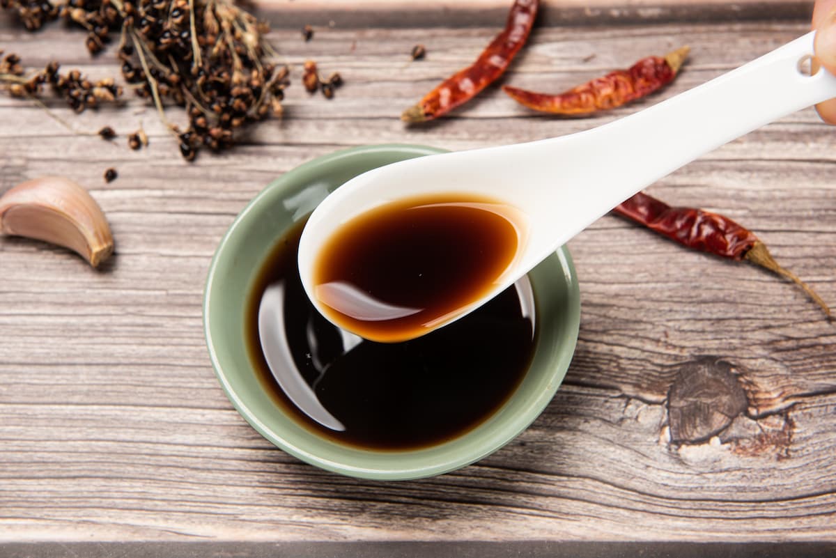 piano di cucina di legno con piattino che contiene la salsa di soia, un cucchiaio cinese e peperoncino e aglio