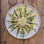 Alici marinate: come si puliscono e come si preparano, la ricetta passo passo 1 su tavolo di legno, piatto bianco con alici marinate, olio Evo e una fetta di limone al centro
