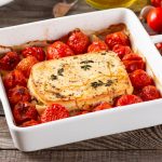 Feta al forno: un piatto vegetariano greco 1 su tavolo di legno, piatto da forno bianco con feta al forno e pomodorini