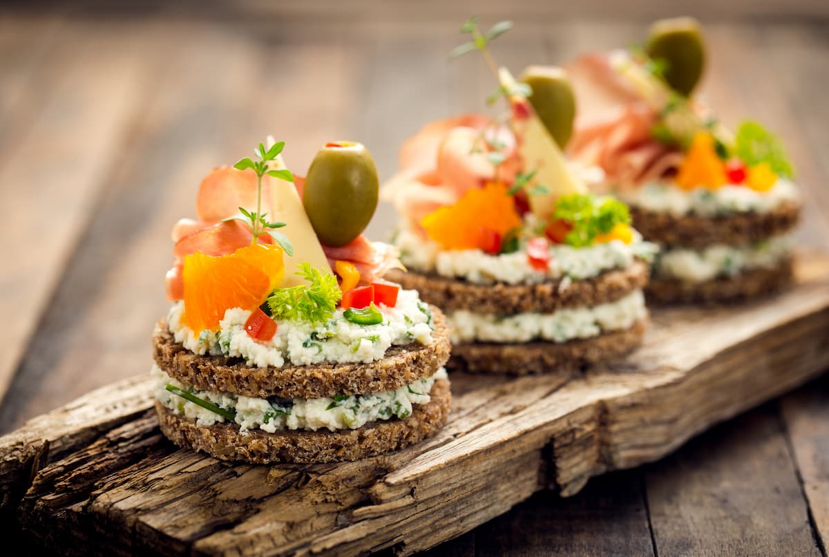 Finger food: ricette veloci di pesce, carne, vegetariane e dolci al cucchiaio 1 su un tagliere di legno 3 finger food con pane integrale formaggio, salmone e olive