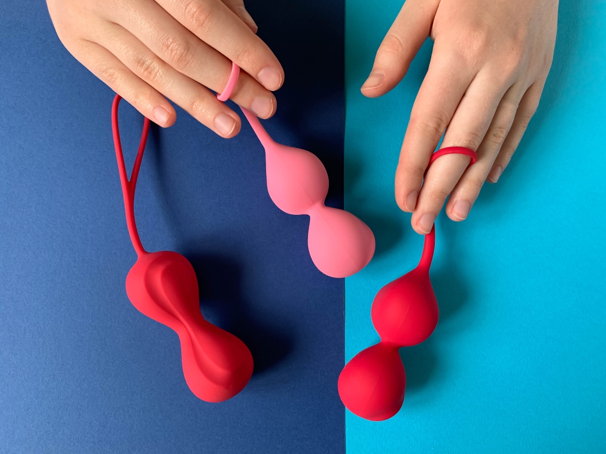 su sfondo blu e azzurro mani di una donna che tiene 3 palline vaginali rose chiare e fucsia.