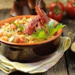 Cous cous di pesce: ricetta e come si prepara il cous cous alla Trapanese 1 pentola di coccio con cous cous di pesce su tavolo di legno