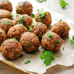 Polpette di lenticchie: un secondo piatto vegetariano 1 su tavolo primo piano di un vassoio con polpette di lenticchie e prezzemolo con sotto carta da forno